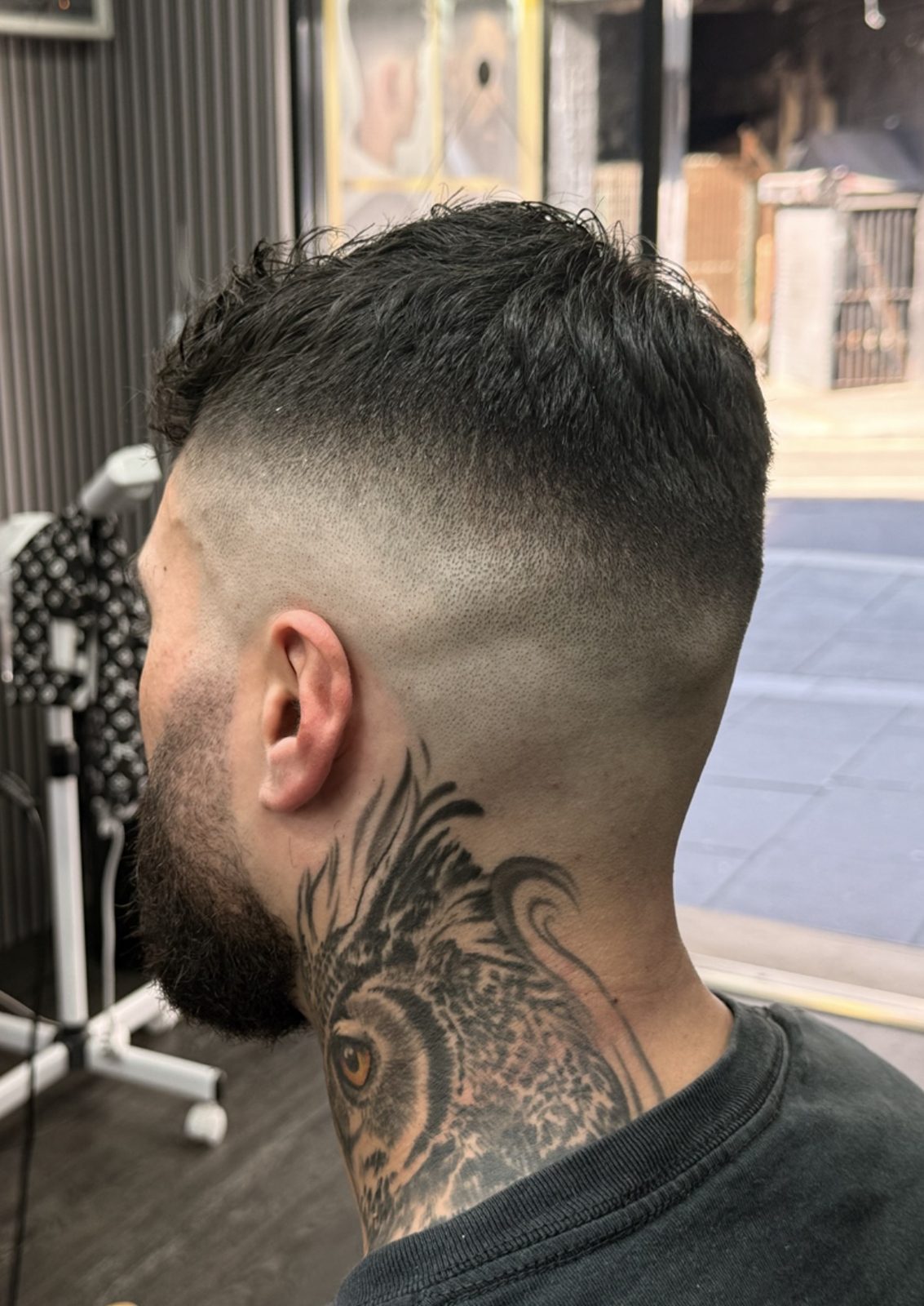 Skin fade with a textured top and a neck tattoo, by the shop window