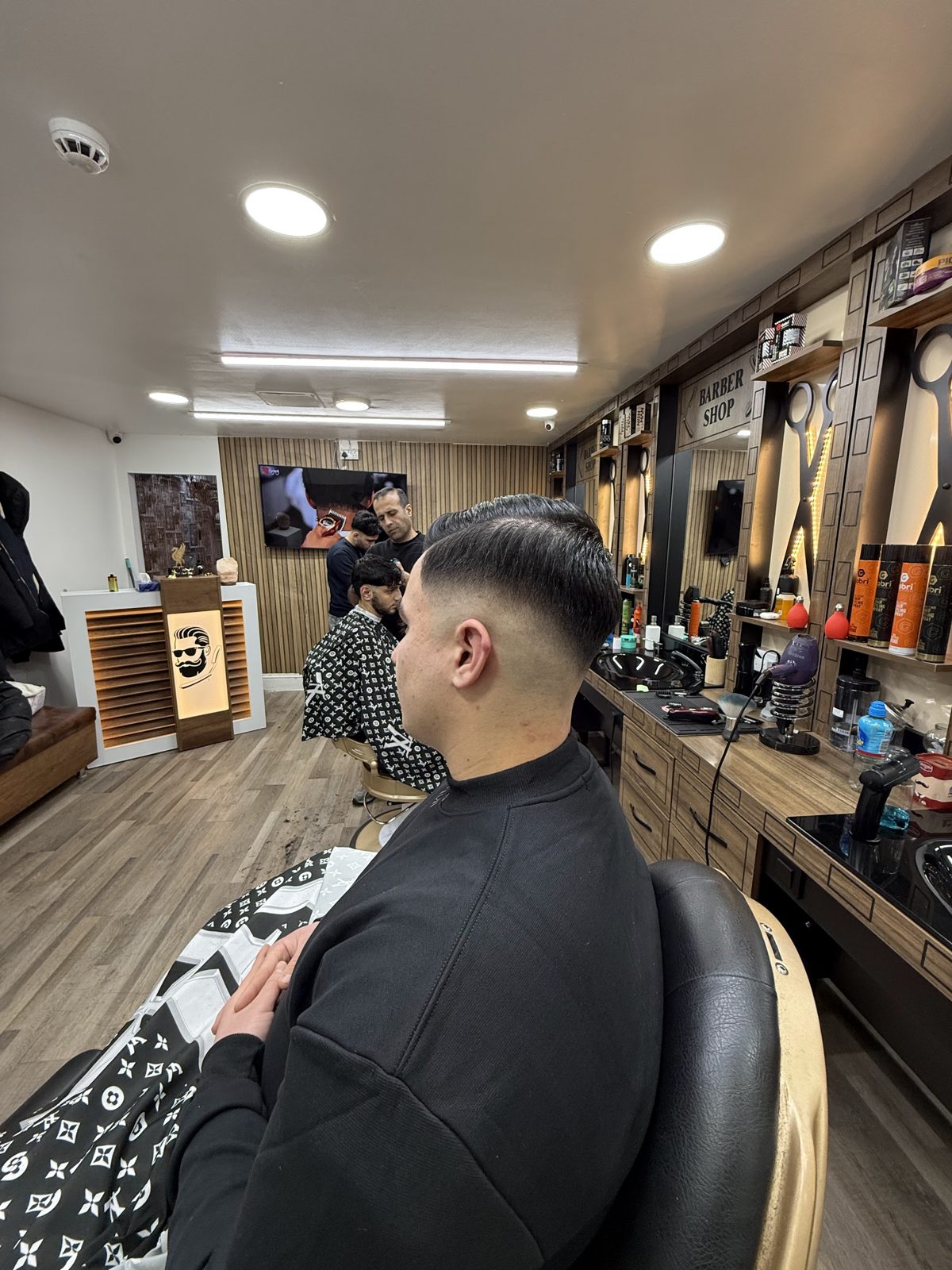 A customer in the chair, with the barber stations and mirrors running down the shop